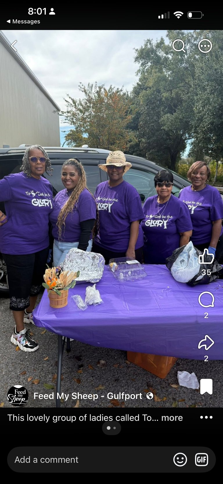 Five women in matching purple Glory t-shirts stand behind a purple table with supplies at an outdoor community event